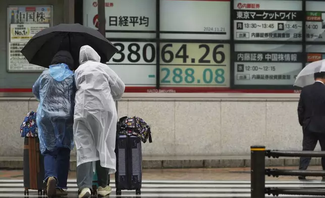 Travelers walk by monitors showing Japan's Nikkei 225 index at a securities firm in Tokyo, Thursday, Nov. 21, 2024. (AP Photo/Hiro Komae)