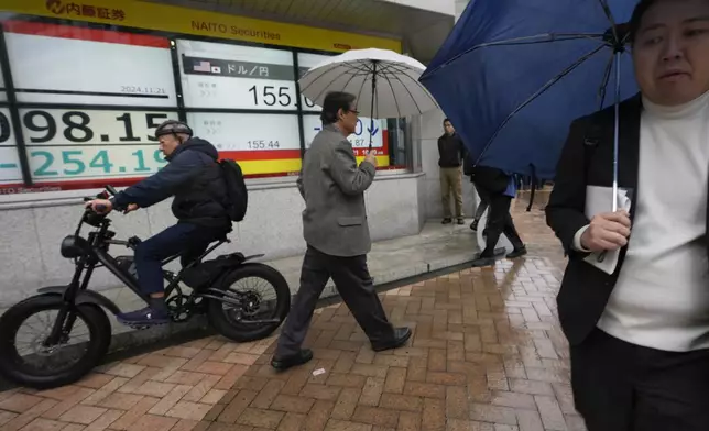 People walk by monitors showing Japan's Nikkei 225 index and Japan's foreign exchange rate against the U.S. dollar at a securities firm in Tokyo, Thursday, Nov. 21, 2024. (AP Photo/Hiro Komae)