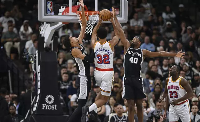 Golden State Warriors' Trayce Jackson-Davis (32) goes to the basket against San Antonio Spurs' Harrison Barnes (40) and Victor Wembanyama, left, during the first half of an NBA basketball game, Saturday, Nov. 23, 2024, in San Antonio. (AP Photo/Darren Abate)