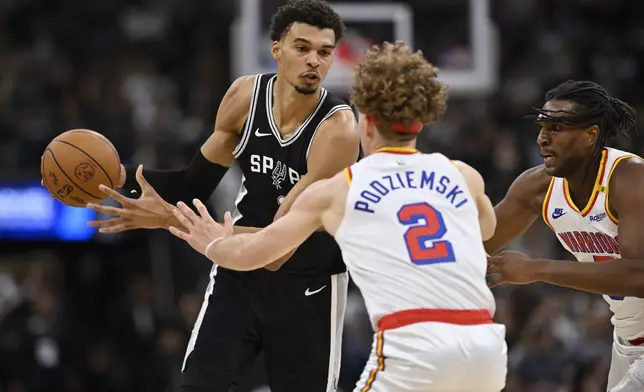 San Antonio Spurs forward Victor Wembanyama, left, drives against Golden State Warriors' Brandin Podziemski (2) and Kevon Looney, right, during the first half of an NBA basketball game, Saturday, Nov. 23, 2024, in San Antonio. (AP Photo/Darren Abate)