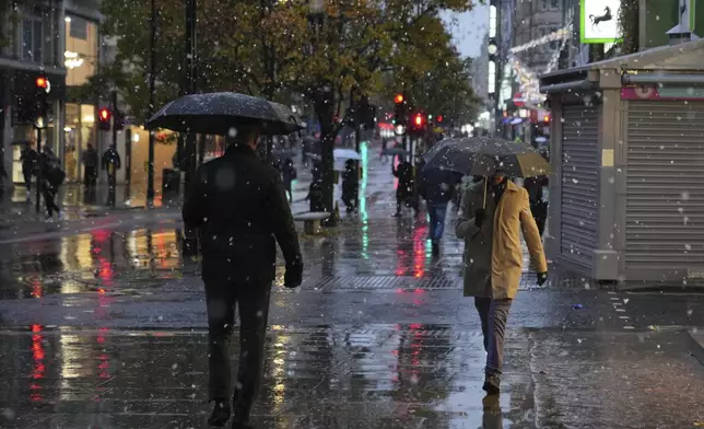 People walk along the Oxford Street as snow falls in London, Tuesday, Nov. 19, 2024. (AP Photo/Kin Cheung)