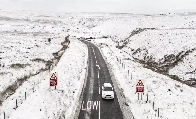 A car moves on the A57 Snake Pass between snowy fields near Glossop, England, Tuesday Nov. 19, 2024. (Danny Lawson/PA via AP)