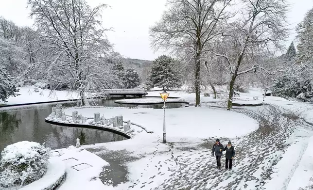 People walk through a park covered in snow after the overnight snowfall in Buxton, Derbyshire, Britain, Tuesday Nov. 19, 2024. (Peter Byrne/PA via AP)