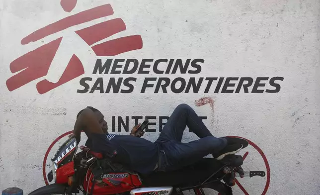 A taxi driver rests on his motorcycle against a facade of a Doctors Without Borders (MSF) clinic in Port-au-Prince, Haiti, Wednesday, Nov. 13, 2024. (AP Photo/Odelyn Joseph)