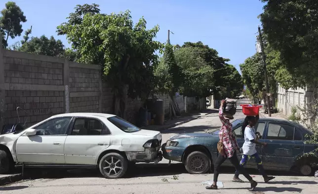 Pedestrians walk past vehicles serving as a barricade set up by residents to deter gang members from entering their neighborhood, in downtown Port-au-Prince, Haiti, Wednesday, Nov. 13, 2024. (AP Photo/Odelyn Joseph)