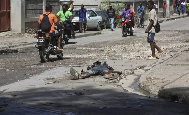 Pedestrians walk past the decomposing body of a man left abandoned on a street in downtown Port-au-Prince, Haiti, Wednesday, Nov. 13, 2024. (AP Photo/Odelyn Joseph)