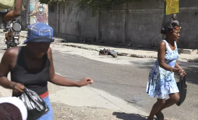 Pedestrians rush past the decomposing body of a man left abandoned on a street in downtown Port-au-Prince, Haiti, Wednesday, Nov. 13, 2024. (AP Photo/Odelyn Joseph)