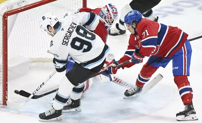 Utah Hockey Club's Mikhail Sergachev (98) scores against Montreal Canadiens goaltender Sam Montembeault as Canadiens' Jake Evans (71) defends during overtime of an NHL hockey game in Montreal, Tuesday, Nov. 26, 2024. (Graham Hughes/The Canadian Press via AP)