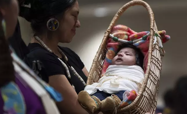 Kimberly Jurado holds her daughter, Delia Rubi Jurado, as they walk during a dance at a powwow at Chinook Winds Casino Resort, Saturday, Nov. 16, 2024, in Lincoln City, Ore. (AP Photo/Jenny Kane)