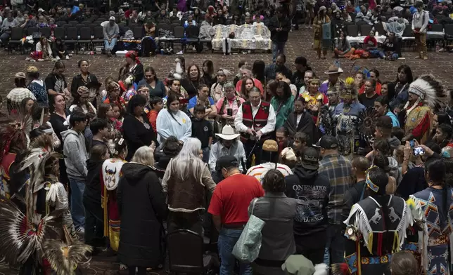 People gather around Chet Clark, in the white hat at center, as he plays an honor song for the Confederated Tribes of Siletz Indians during a powwow at Chinook Winds Casino Resort, Saturday, Nov. 16, 2024, in Lincoln City, Ore. Chet, of the drum group Johonaaii, wrote the song in 2007 and sang it for the first time during the tribe's 30th restoration powwow. It has been sung during every restoration powwow since then. (AP Photo/Jenny Kane)