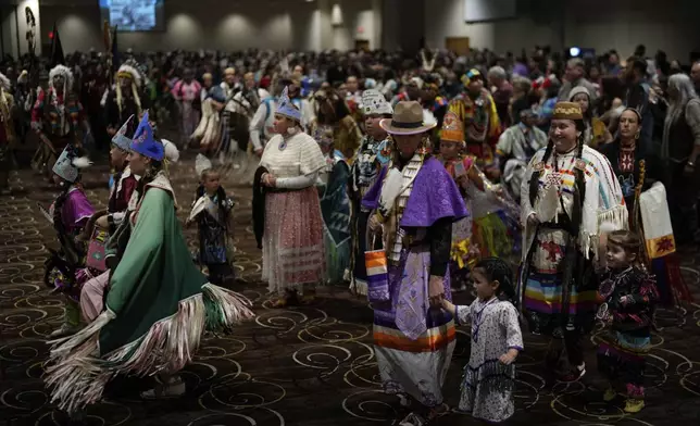 Tiffany Stuart, at right in white, holds hands with her daughter Kwestaani Chuski Stuart, bottom right, as they participate in a powwow at Chinook Winds Casino Resort, Saturday, Nov. 16, 2024, in Lincoln City, Ore. (AP Photo/Jenny Kane)