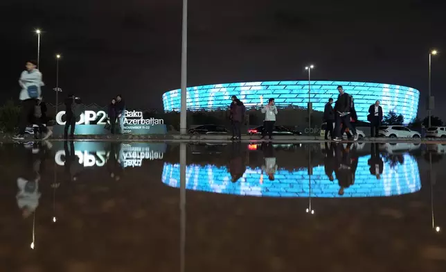 People pose for a picture with the Baku Olympic Stadium in the background during the COP29 U.N. Climate Summit, Monday, Nov. 18, 2024, in Baku, Azerbaijan. (AP Photo/Rafiq Maqbool)