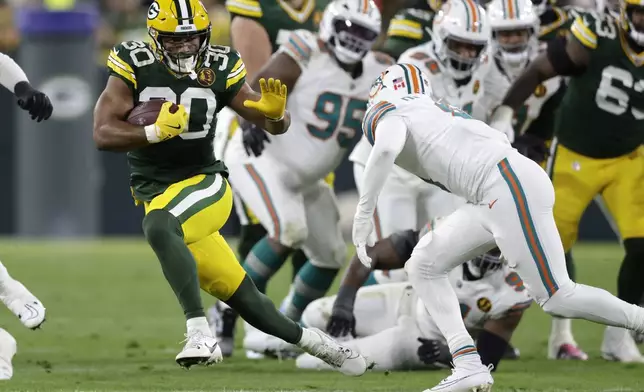 Green Bay Packers running back Chris Brooks (30) runs from Miami Dolphins safety Jevon Holland, right, during the first half of an NFL football game Thursday, Nov. 28, 2024, in Green Bay, Wis. (AP Photo/Matt Ludtke)