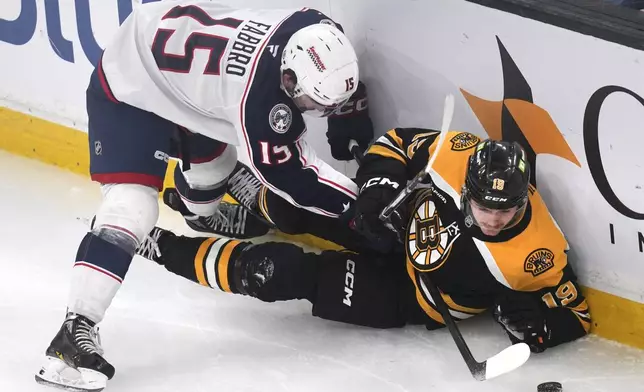 Boston Bruins center John Beecher (19) tries to keep control of the puck against Columbus Blue Jackets defenseman Dante Fabbro (15) during the first period of an NHL hockey game, Monday, Nov. 18, 2024, in Boston. (AP Photo/Charles Krupa)