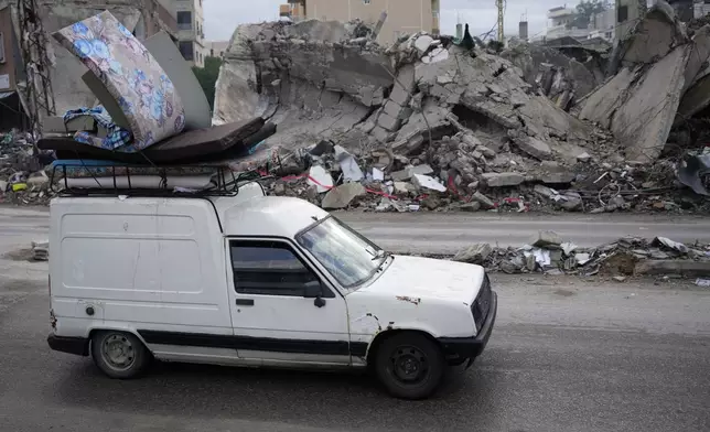 People in a car return back to their villages with their belongings after a ceasefire between Hezbollah and Israel began early morning, as they pass in front of a destroyed building that was hit in an Israeli airstrike, in Tyre, south Lebanon, Wednesday, Nov. 27, 2024. (AP Photo/Hussein Malla)