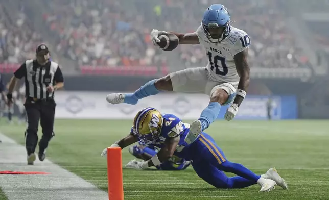 Toronto Argonauts' Kevin Mital (10) leaps to evade a hit from Winnipeg Blue Bombers' Terrell Bonds (24) and scores a touchdown during the second half of a CFL football game at the 111th Grey Cup in Vancouver, British Columbia, Sunday, Nov. 17, 2024. (Darryl Dyck/The Canadian Press via AP)