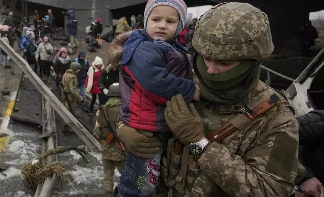 FILE - A Ukrainian serviceman holds a child crossing the Irpin river on an improvised path under a bridge, that was destroyed by Ukrainian troops designed to slow any Russian military advance, while assisting people fleeing the town of Irpin, Ukraine, on March 5, 2022. (AP Photo/Vadim Ghirda, File)