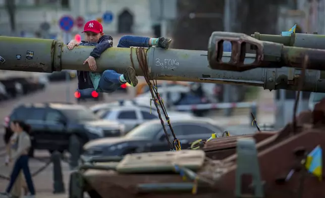 FILE - A boy holds on to the barrel of a tank, part of a display of destroyed Russian military equipment, in Kyiv, Ukraine, Sunday, March 31, 2024. (AP Photo/Vadim Ghirda, File)