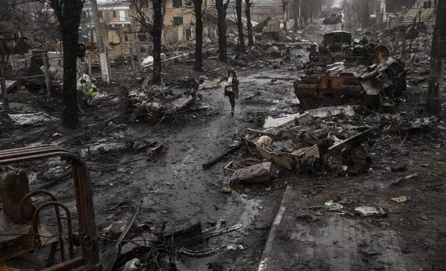 FILE - A woman walks amid destroyed Russian tanks in Bucha, in the outskirts of Kyiv, Ukraine, Sunday, April 3, 2022. (AP Photo/Rodrigo Abd, File)