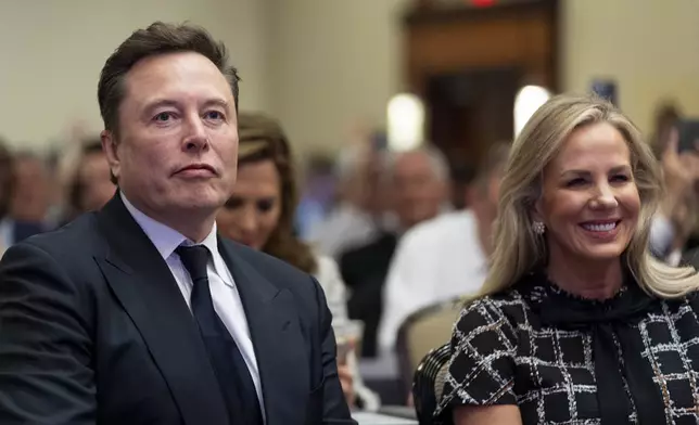 Elon Musk, left, sits with Kelly Johnson, wife of House Speaker Mike Johnson of La., as President-elect Donald Trump speaks at a meeting of the House GOP conference, Wednesday, Nov. 13, 2024, in Washington. (AP Photo/Alex Brandon)