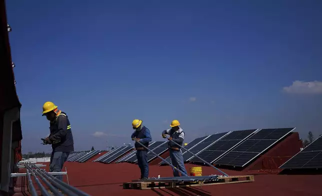 FILE - Workers install solar panels on the roof of "El Central de Abastos," the largest whole-sale food and goods market in Mexico City, Aug. 3, 2022. (AP Photo/Fernando Llano, File)