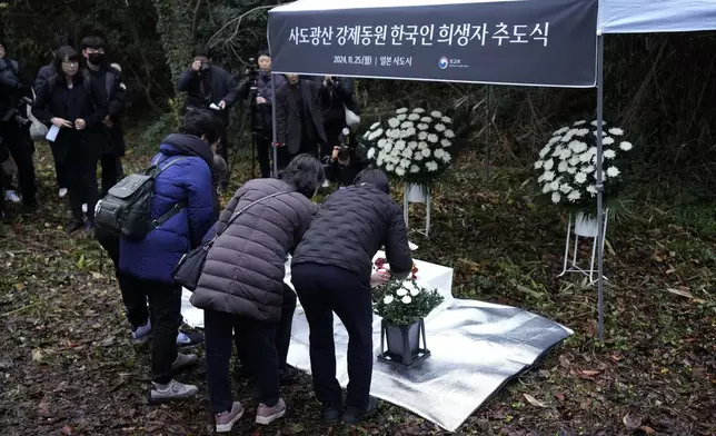 Relatives of Korean victims and South Korean officials offer flowers during a memorial service in Sado, Niigata prefecture, Japan, Monday, Nov. 25, 2024, after boycotting a memorial organized by Japanese officials. The black banner reads " A memorial service for Korean forced laborer victims at Sado Mine." (AP Photo/Eugene Hoshiko)