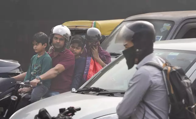 A family on a motorcycle waits at a traffic signal surrounded by smog in New Delhi, India, Thursday, Nov. 14, 2024. (AP Photo/Manish Swarup)