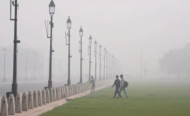 A worker sweeps a pathway surrounded by a thick layer of smog in New Delhi, India, Thursday, Nov. 14, 2024. (AP Photo/Manish Swarup)