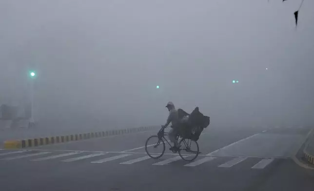 A cyclist crosses a road as smog envelopes the area of Lahore, Pakistan, Thursday, Nov. 14, 2024. (AP Photo/K.M. Chaudary)