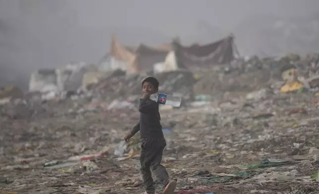 A boy walks with drinking water as smoke rises from a garbage dump on the outskirts of Jammu, India, Thursday, Nov.14, 2024. (AP Photo/Channi Anand)