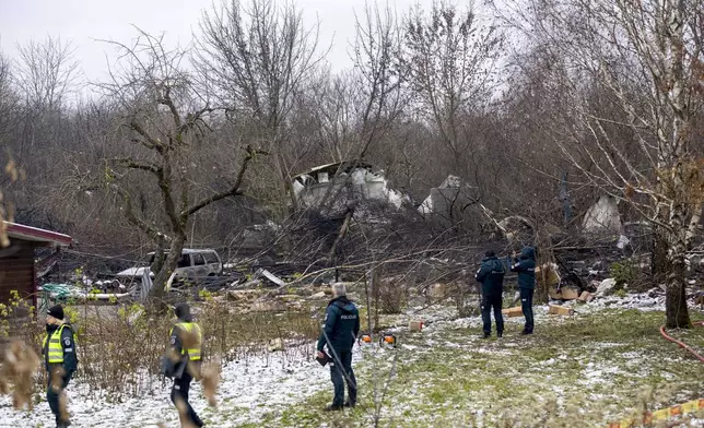 Lithuanian Emergency Ministry employees and police officers stand near the place where a DHL cargo plane crashed into a house near the Lithuanian capital Vilnius, Lithuania, Lithuania, Monday, Nov. 25, 2024. (AP Photo/Mindaugas Kulbis)