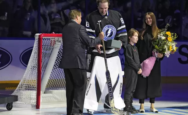 Tampa Bay Lightning owner Jeff Vinik, left, present goaltender Andrei Vasilevskiy with a gold stick before an NHL hockey game Saturday, Nov. 16, 2024, after Vasilevskiy won his 300th game earlier this week in Tampa, Fla. Looking on is his wife Ksenia and son Lukas. (AP Photo/Chris O'Meara)