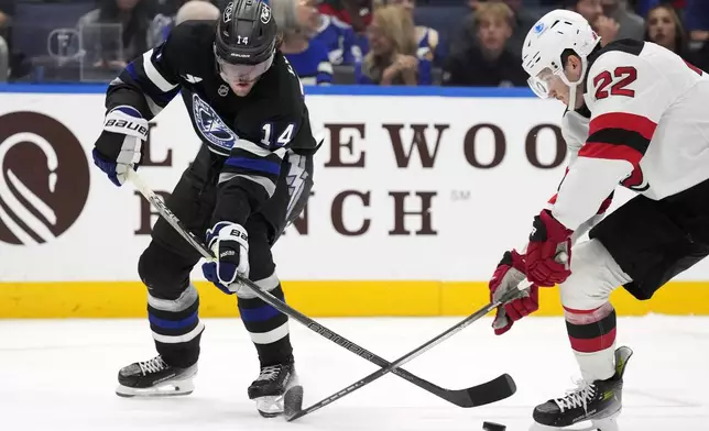 New Jersey Devils defenseman Brett Pesce (22) strips the puck from Tampa Bay Lightning center Conor Geekie (14) during the second period of an NHL hockey game Saturday, Nov. 16, 2024, in Tampa, Fla. (AP Photo/Chris O'Meara)