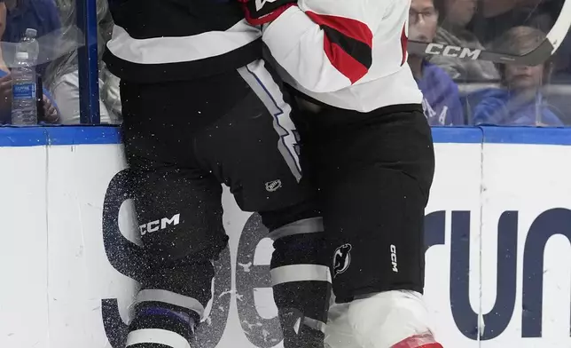 New Jersey Devils left wing Kurtis MacDermid (23) checks Tampa Bay Lightning defenseman Darren Raddysh (43) inito the boards during the first period of an NHL hockey game Saturday, Nov. 16, 2024, in Tampa, Fla. (AP Photo/Chris O'Meara)