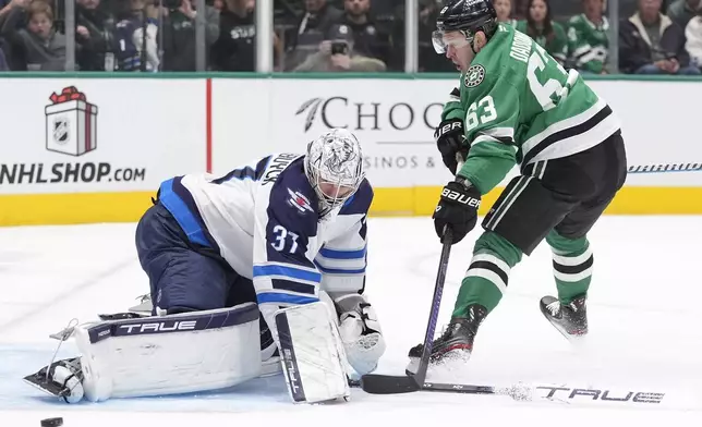 Winnipeg Jets goaltender Connor Hellebuyck (37) defends the goal against Dallas Stars right wing Evgenii Dadonov (63) during the first period of an NHL hockey game Sunday, Dec. 1, 2024, in Dallas. (AP Photo/LM Otero)