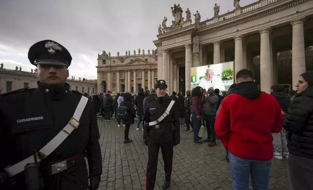 Carabinieri police officers patrol as people look at giant screens in St.Peter's Square showing Pope Francis reciting the Angelus noon prayer from his Santa Marta Residence, after he decided not to appear at the window of his studio overlooking the square because of a persistent cold, at the Vatican, Sunday, Dec. 22, 2024. (AP Photo/Andrew Medichini)