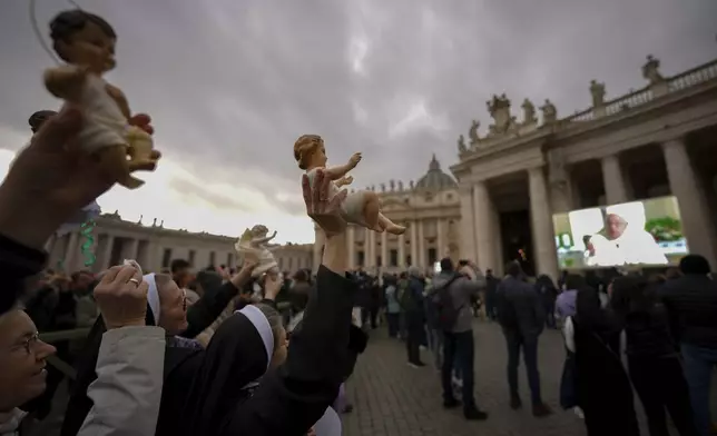 People hold statuettes of baby Jesus as they look at a giant screen in St.Peter's Square, at the Vatican, showing Pope Francis reciting the Angelus noon prayer from his Santa Marta Residence, after he decided not to appear at the window of his studio overlooking the square because of a persistent cold, Sunday, Dec. 22, 2024. (AP Photo/Andrew Medichini)