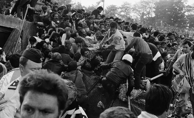 FILE - A crowd of soccer fans try to escape a collapsed wall prior to the start of the European Cup final between Liverpool and Juventus, at the Heysel Stadium in Brussels, May 29, 1985. (AP Photo/Gianni Foggia, File)