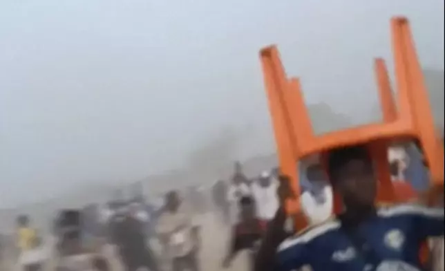 In this grab taken from video provided by Nimba Sports Zaly, a man holds a chair on top of his head in a stampede, during a soccer match at the Stade de Nzérékoré, in Nzérékoré, Guinea on Sunday, Dec. 1, 2024. (Nimba Sports Zaly via AP)