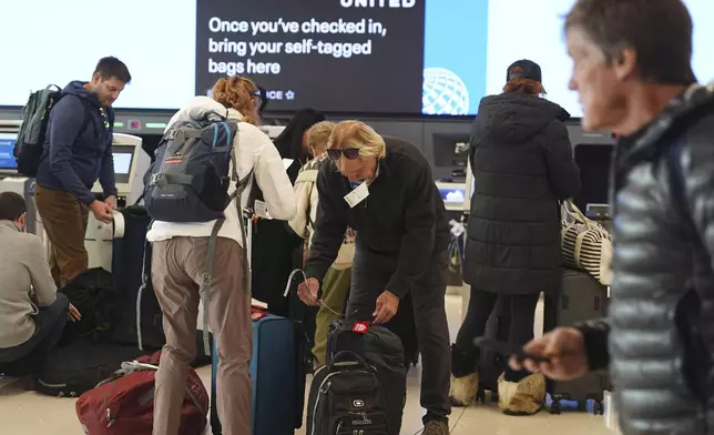 Travelers attach tags to their bags after checking in at the United Airlines counter at Denver International Airport, Saturday, Dec. 14, 2024, in Denver. (AP Photo/David Zalubowski)