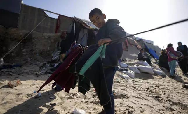 A Palestinian child hanging cloths on a rope outside tents made locally from pieces of cloth and nylon, in a camp for internally displaced Palestinians at the beachfront in Deir al-Balah, central Gaza Strip, Friday, Dec. 27, 2024. (AP Photo/Abdel Kareem Hana)