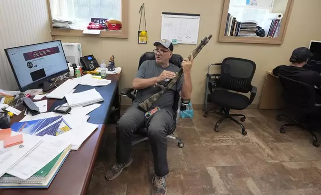 Ron Hubbard, owner of Atlas Survival Shelters, handles a shotgun during an interview at his company's office in Sulphur Springs, Texas, Tuesday, Aug. 27, 2024, (AP Photo/LM Otero)