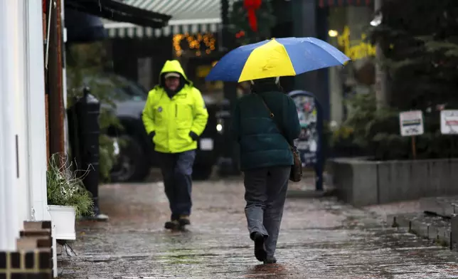 People walk through the rain as a storm system and possible "bomb cyclone" hit the U.S. East Coast, Wednesday, Dec. 11, 2024 in Portsmouth, N.H. (AP Photo/Caleb Jones)