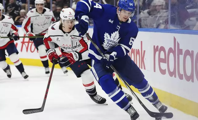 Toronto Maple Leafs' David Kampf (64) protects the puck from Washington Capitals' Jakob Chychrun (6) during second-period NHL hockey game action in Toronto, Saturday, Dec. 28, 2024. (Frank Gunn/The Canadian Press via AP)