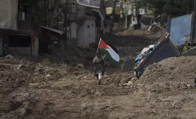 Palestinian activist Khairi Hanoon walks with the Palestinian flag on a damaged road following an Israeli army raid in Tulkarem, West Bank, on Sept. 3, 2024. (AP Photo/Majdi Mohammed)