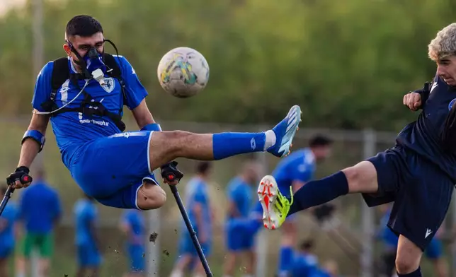 Wearing a device that measures his energy consumption, Israel Amputee Football Team player Ben Maman, left, fights for the ball with a young soccer player from a local team during a practice session in Ramat Gan, Israel, on April 11, 2024. (AP Photo/Leo Correa)