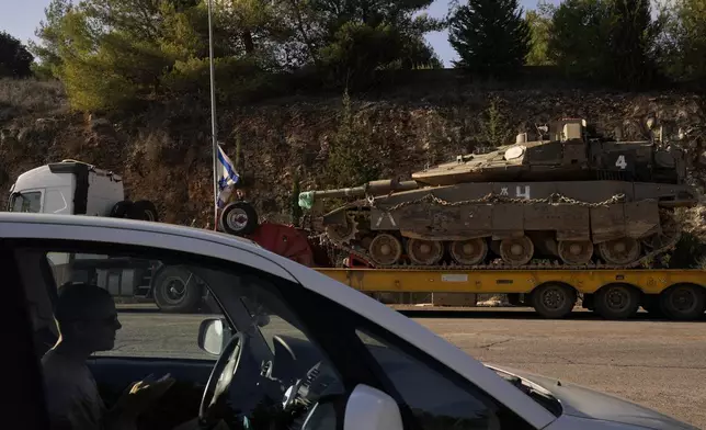 A man waits in his car as an Israeli tank is moved by a truck in northern Israel near the border with Lebanon, Thursday, Dec. 5, 2024. (AP Photo/Matias Delacroix)