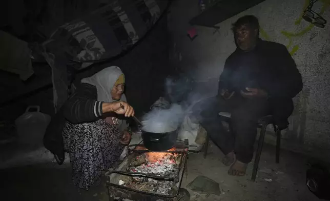 Palestinian Yusuf Sobuh, 60, left, cooks noodles as her husband sits next, in their tent set up on an area in Deir al-Balah, Gaza Strip Thursday, Dec. 5, 2024. (AP Photo/Abdel Kareem Hana)