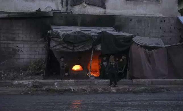 Displaced Palestinians sit next to a makeshift oven on a tent set up on an area in Deir al-Balah, Gaza Strip Thursday, Dec. 5, 2024. (AP Photo/Abdel Kareem Hana)