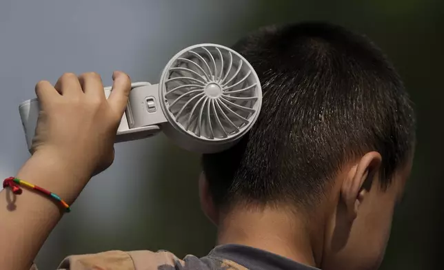 FILE - A boy cools himself with an electric fan on a sweltering day at a park in Tongzhou, on the outskirts of Beijing, June 10, 2024. (AP Photo/Andy Wong, File)